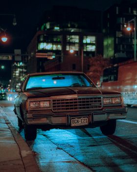 A vintage Chevrolet Caprice parked on a city street at night with neon lights creating a retro atmosphere.