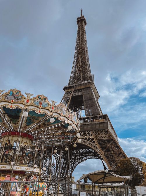 Free A beautiful view of the Eiffel Tower and a colorful Parisian carousel against a cloudy sky. Stock Photo
