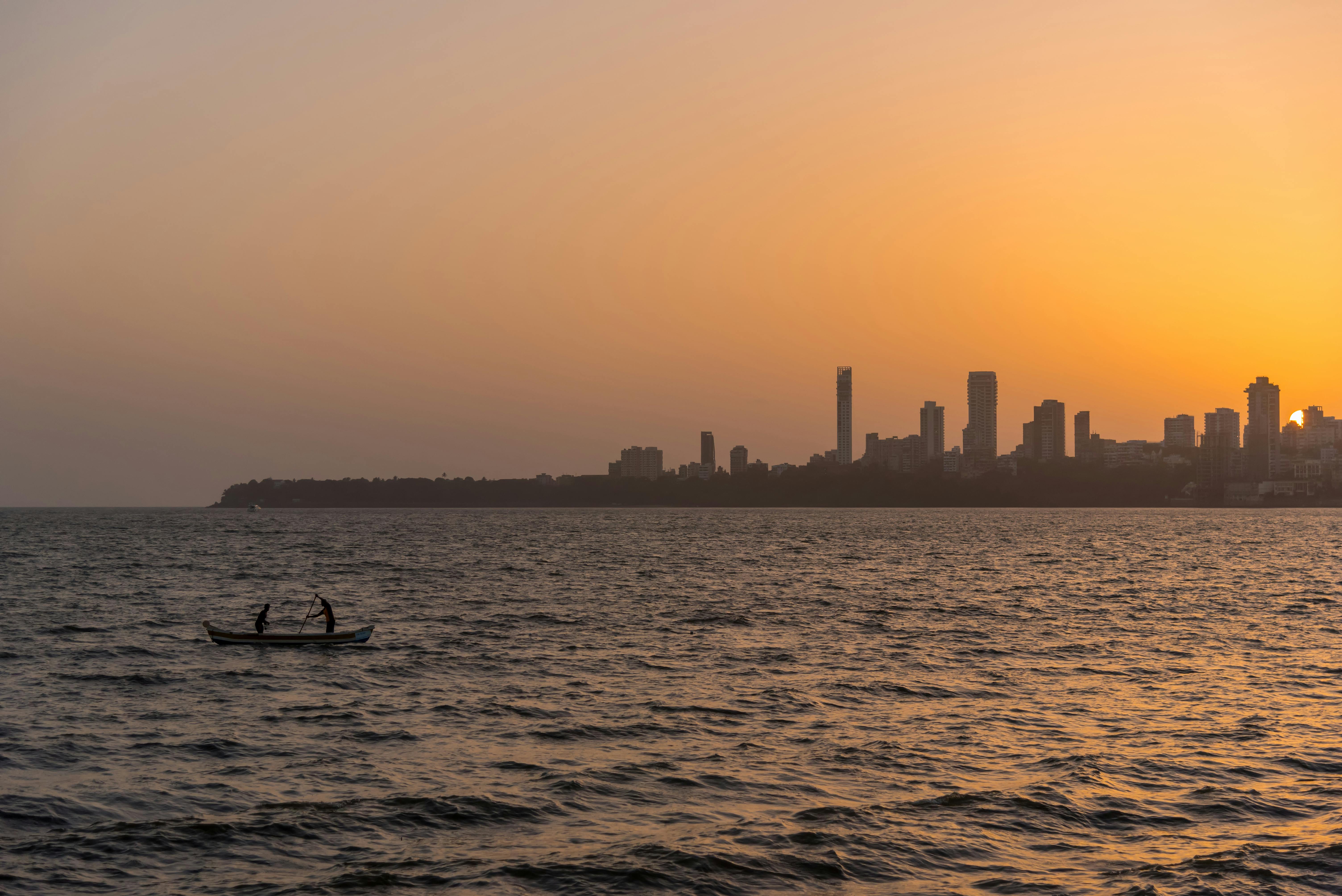 2 Person on the Boat on the Ocean in Front Urban City during Golden Hour