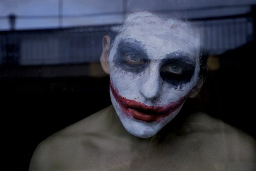 Photo of a Man in a Joker Halloween Makeup Standing behind a Window 