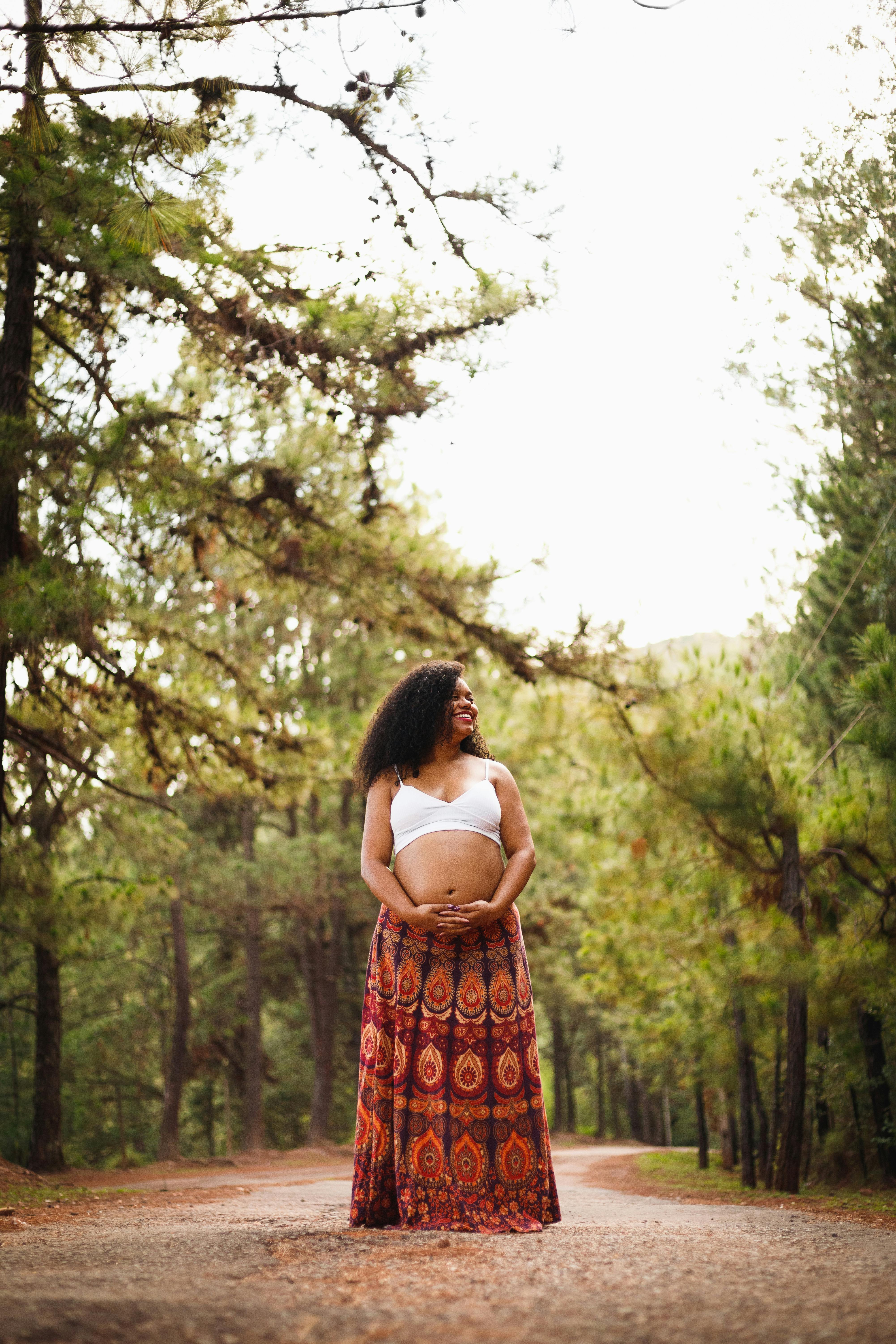 pregnant woman standing in the middle of a forest road