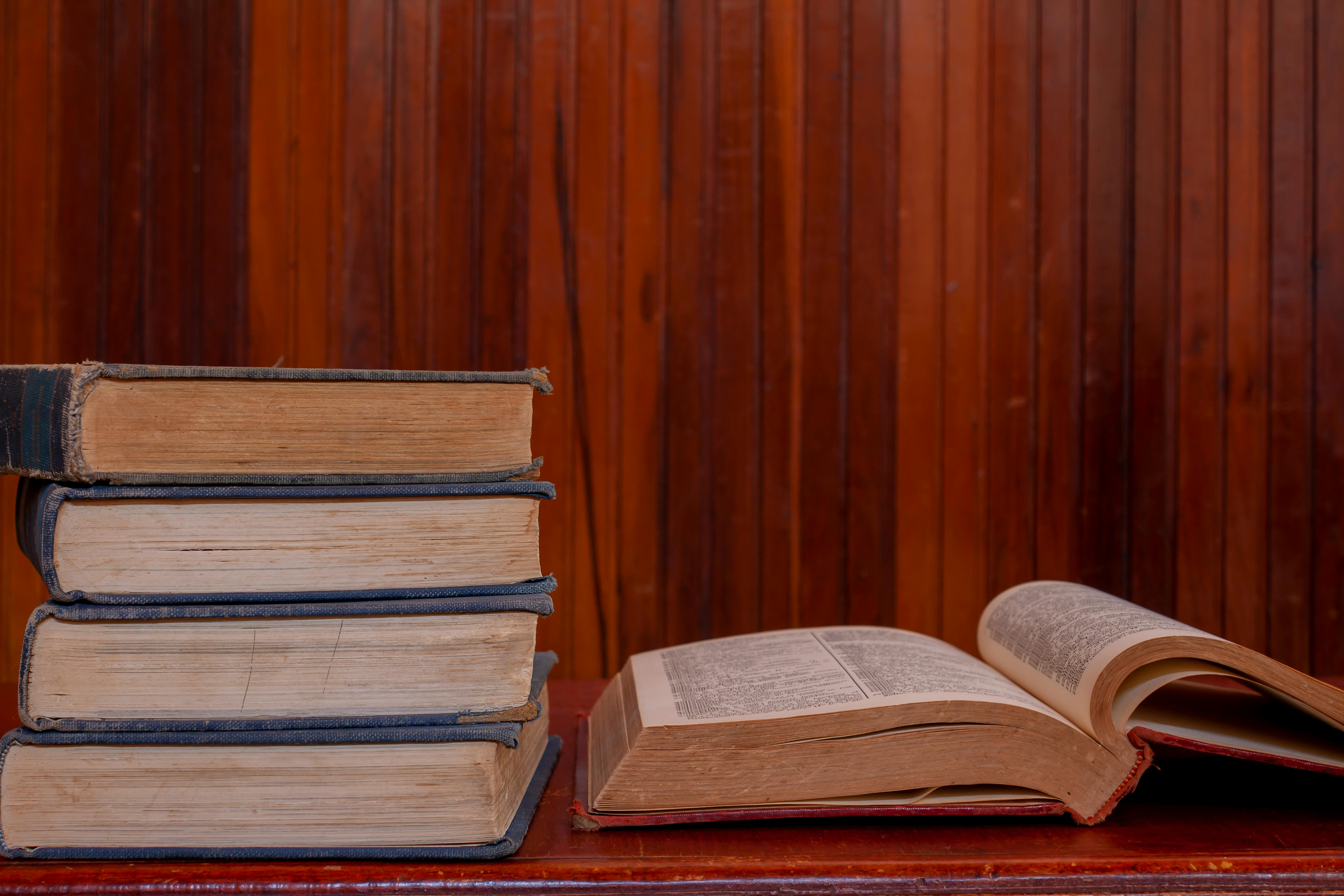 an old book on a wooden table with a stack of books