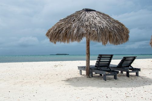 Free Peaceful beach scene with straw umbrella and empty lounge chairs by the sea. Stock Photo