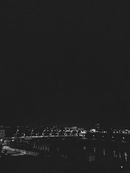 Black and white cityscape of Hrodna at night with lights reflecting on a river.