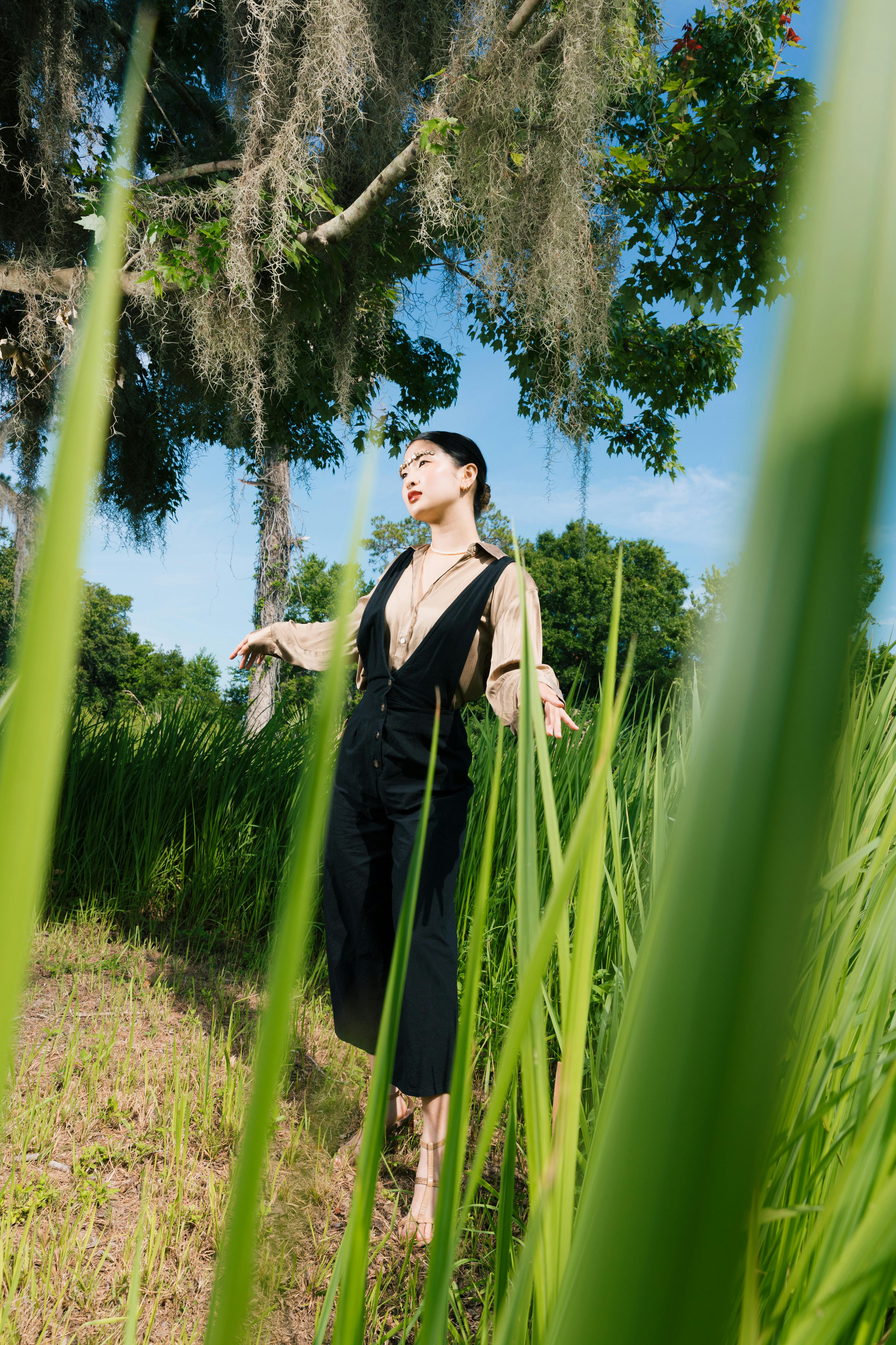 Fashionable woman poses gracefully in lush green surroundings on a sunny day.