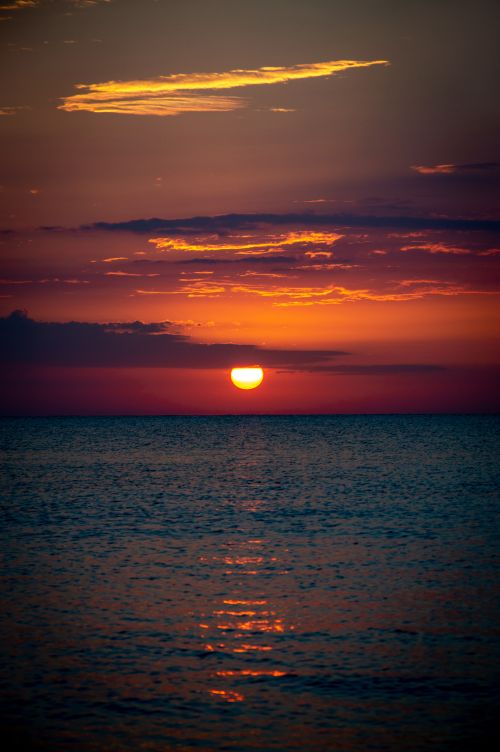 Free Breathtaking view of the sun setting over the ocean with vivid hues and calm waters. Stock Photo