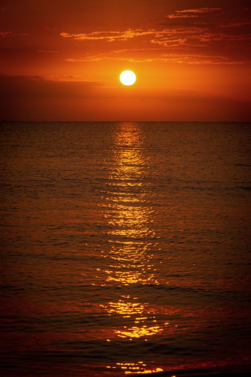 Free A captivating view of the sun setting over the ocean with a vibrant red sky and shimmering water reflections. Stock Photo