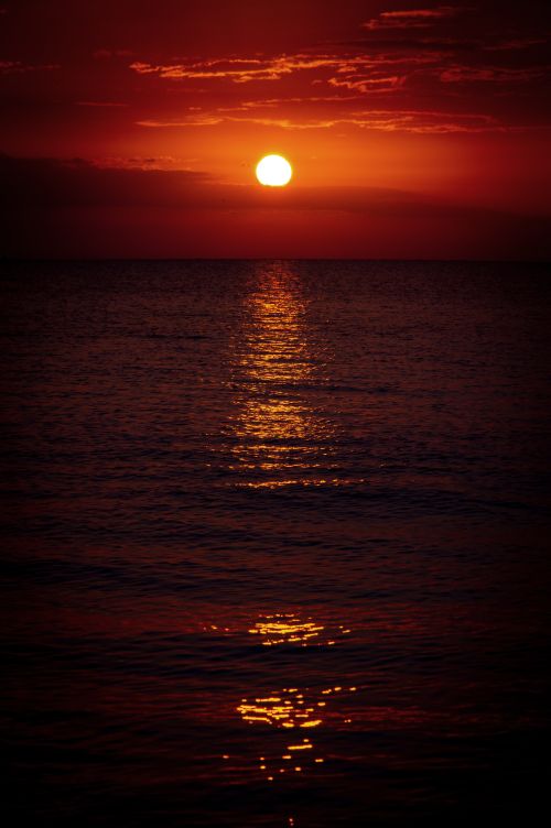 Free A captivating sunset over the ocean, casting a warm glow on the water's surface and highlighting the red sky. Stock Photo