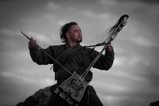Traditional musician playing a morin khuur outdoors, showcasing cultural heritage and the art of music in nature.