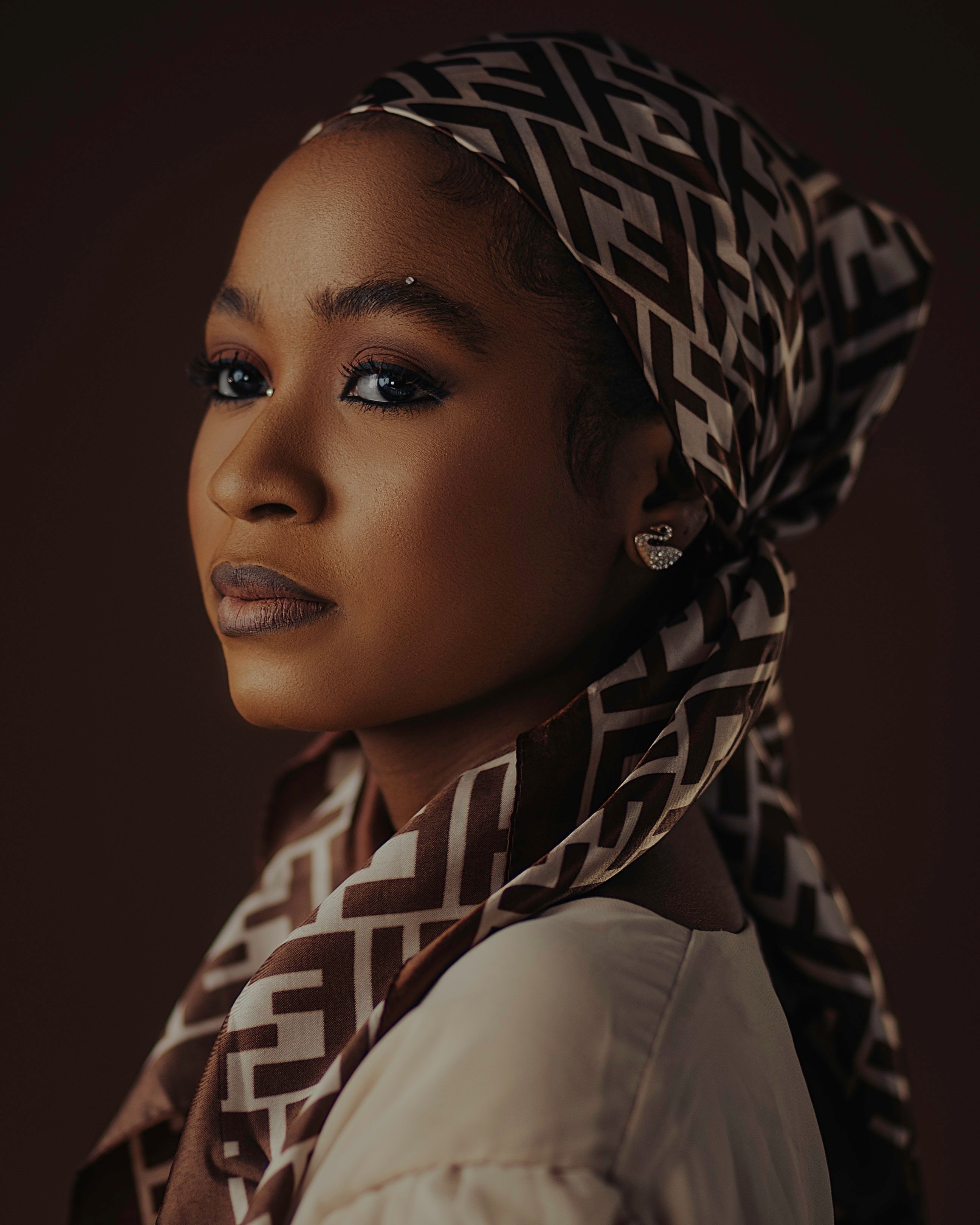 Close-up portrait of an elegant African woman wearing a patterned headscarf, studio lighting.