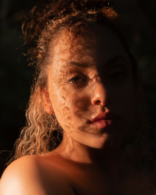 Free Portrait of a young woman with curly hair in dynamic light and shadow. Stock Photo