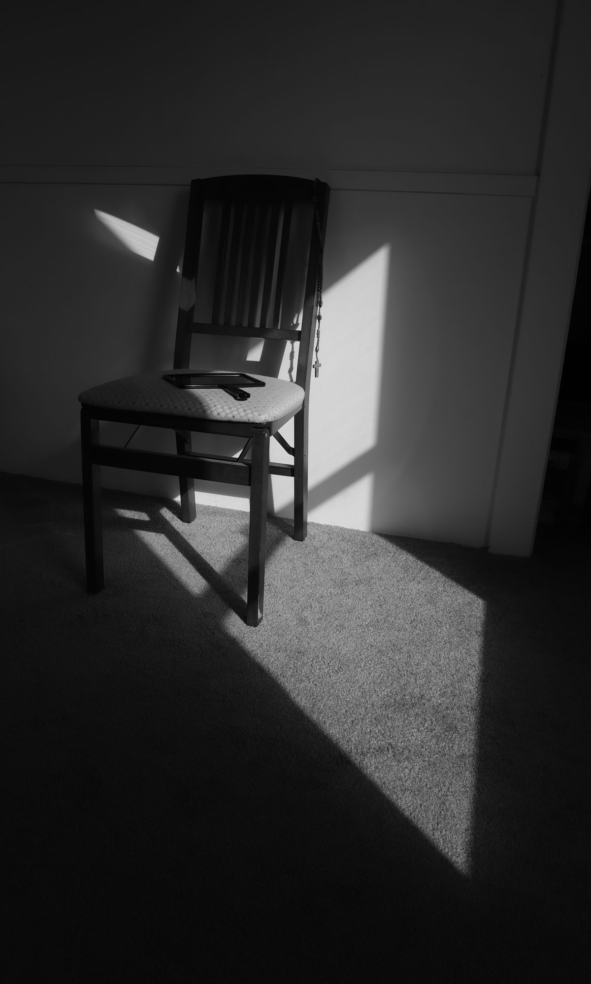 A black and white photo of a single chair in an empty sunlit room.