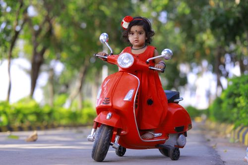 Free A young girl in a red dress riding a toy scooter in a sunny park. Stock Photo