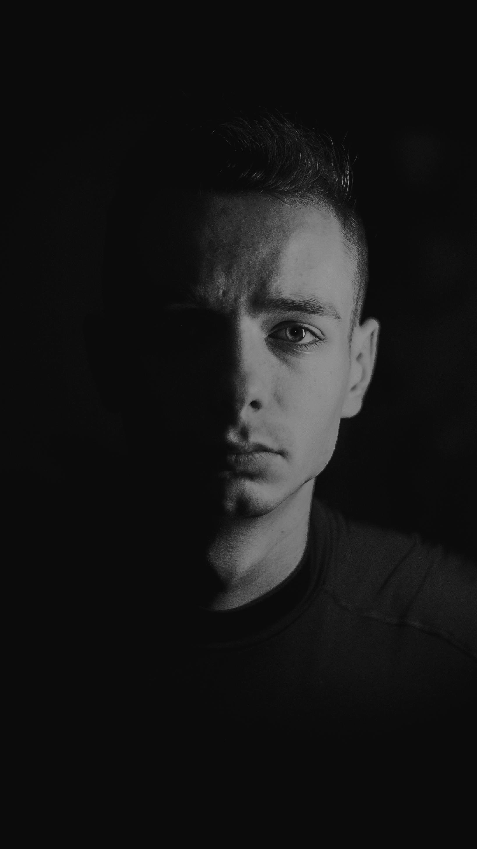 Moody black and white portrait of a man with short hair against a dark background.