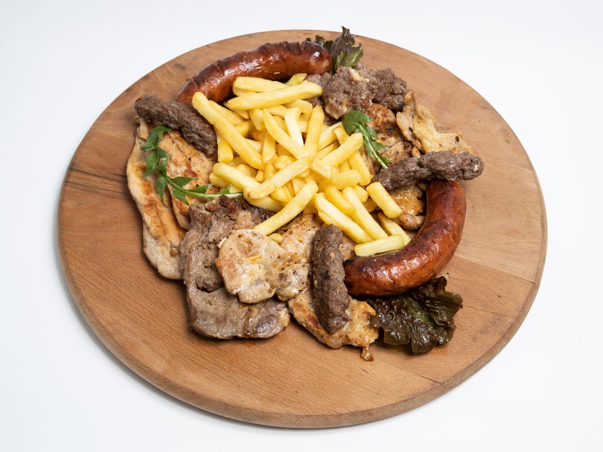 A mixed grill platter of meats and sausages with fries on a wooden board.