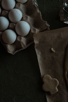 Moody tabletop shot of eggs in a carton and dough on parchment paper.