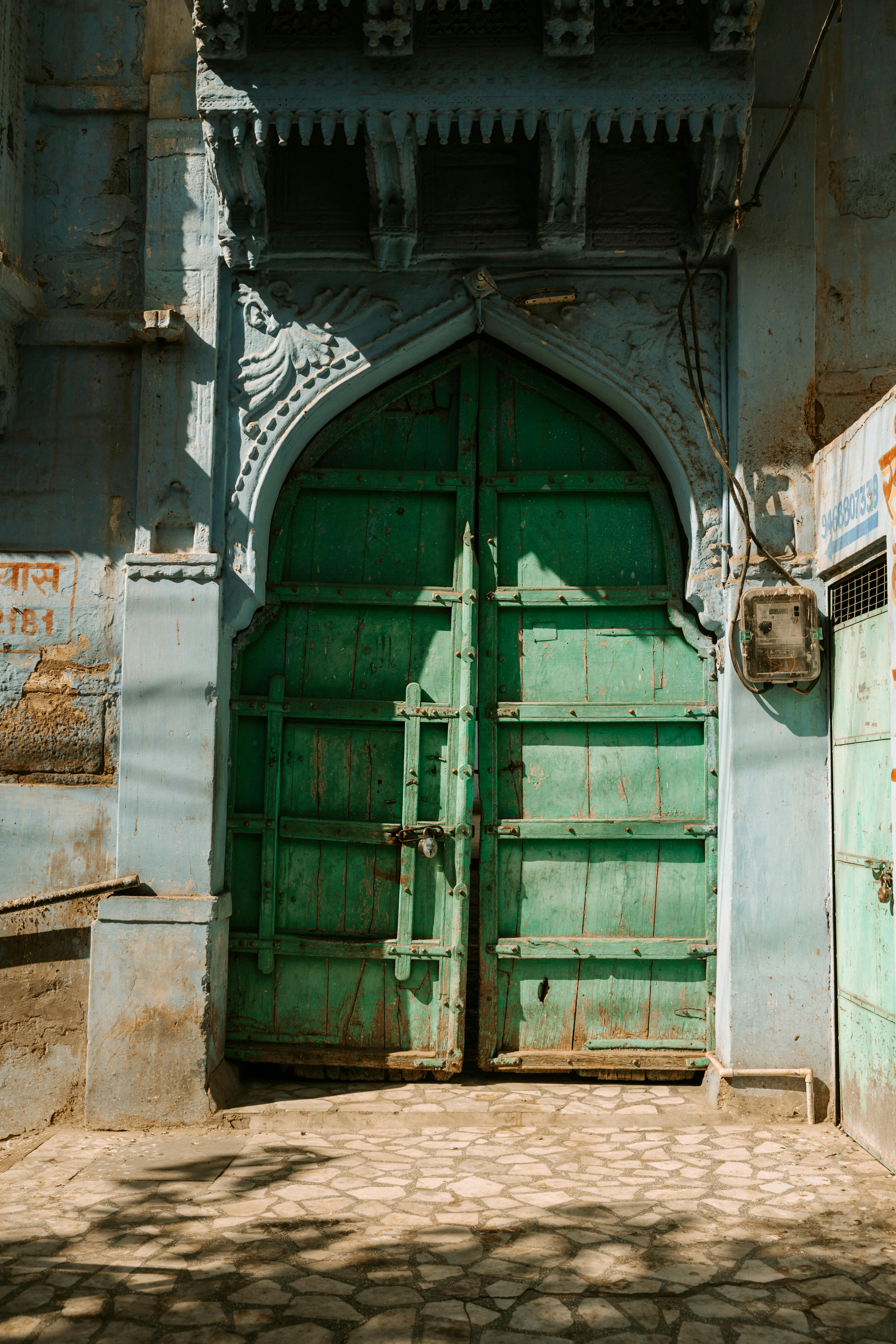 Sunlit green wooden gate with ornate arch in India, creating a vibrant architectural scene.