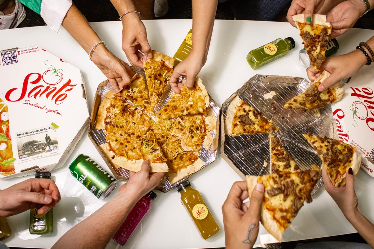Top view of friends sharing pizza slices with drinks around a table