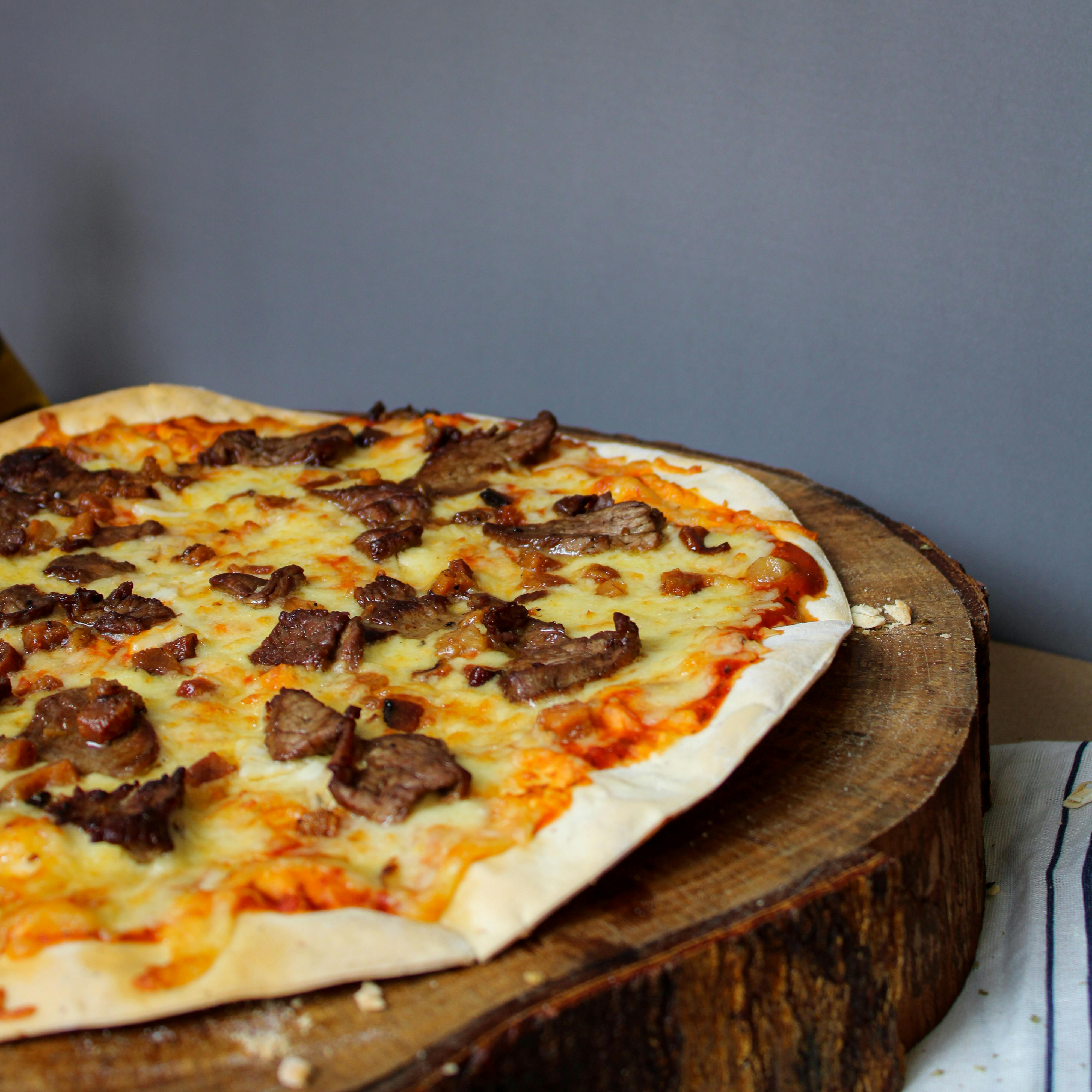 Delicious beef pizza with melted cheese served on a rustic wooden board against a gray background.