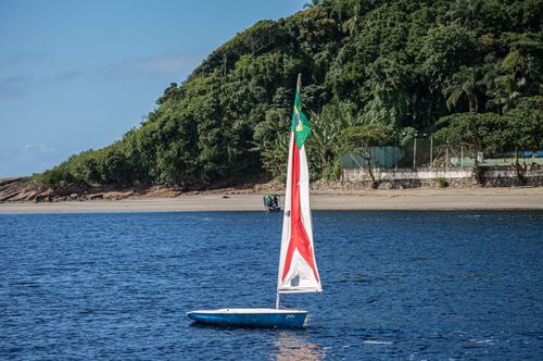 Free A sailboat floats near a lush, green coastline under a clear blue sky, capturing the essence of a summer day. Stock Photo