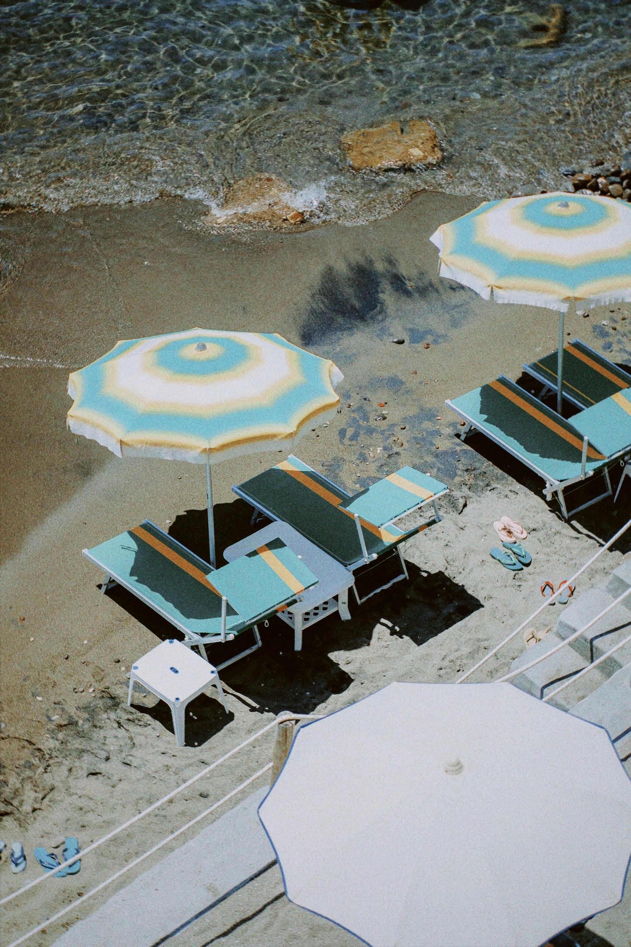A serene top-down view of beach umbrellas and sunbeds on a tranquil sandy shore by the sea.