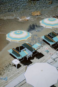 A serene top-down view of beach umbrellas and sunbeds on a tranquil sandy shore by the sea.