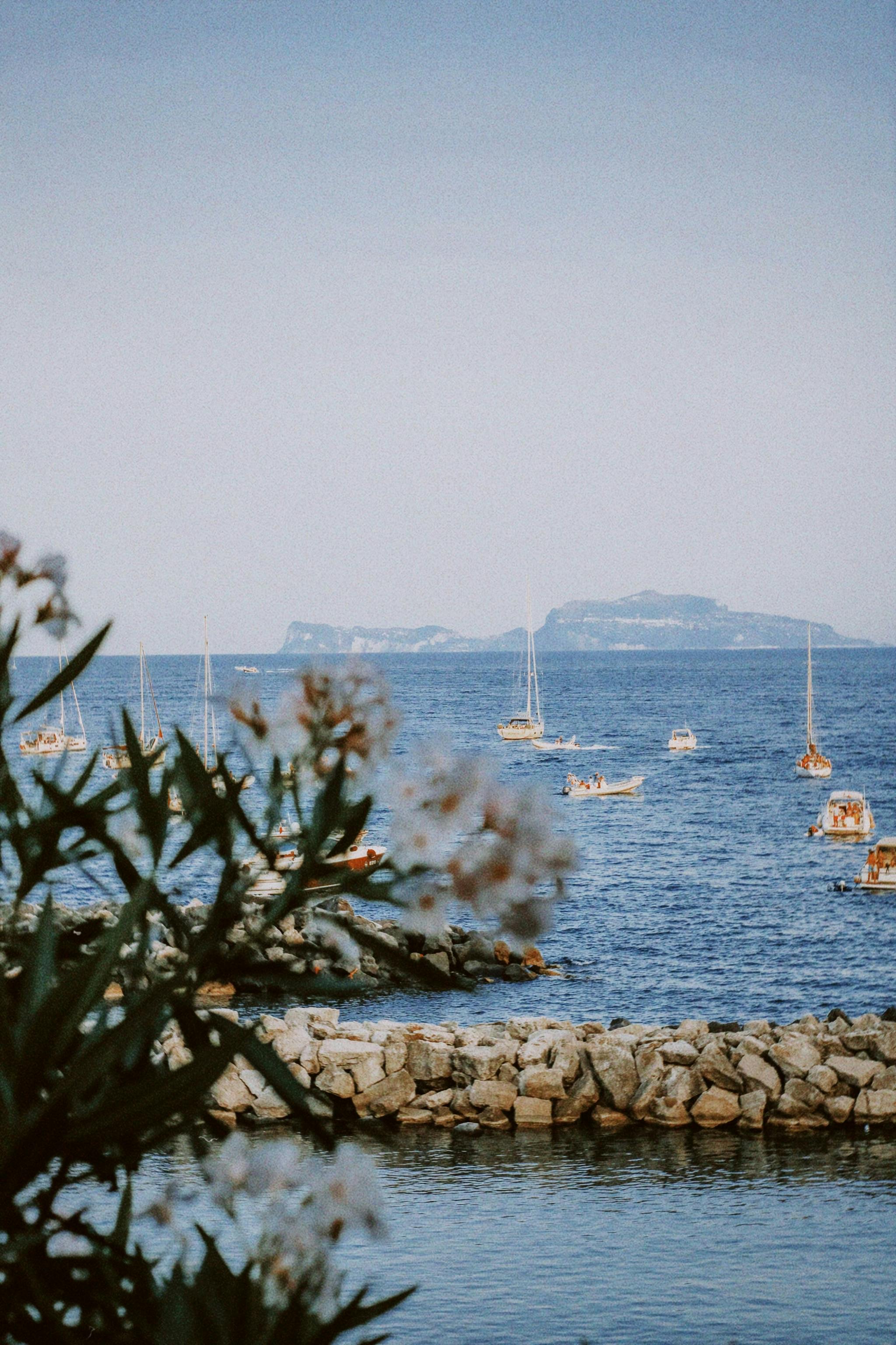 Idyllic coastal scene with sailboats and rocky shoreline, capturing tranquility.