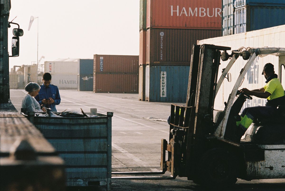 Workers operating a forklift in a shipping-container yard at an African port