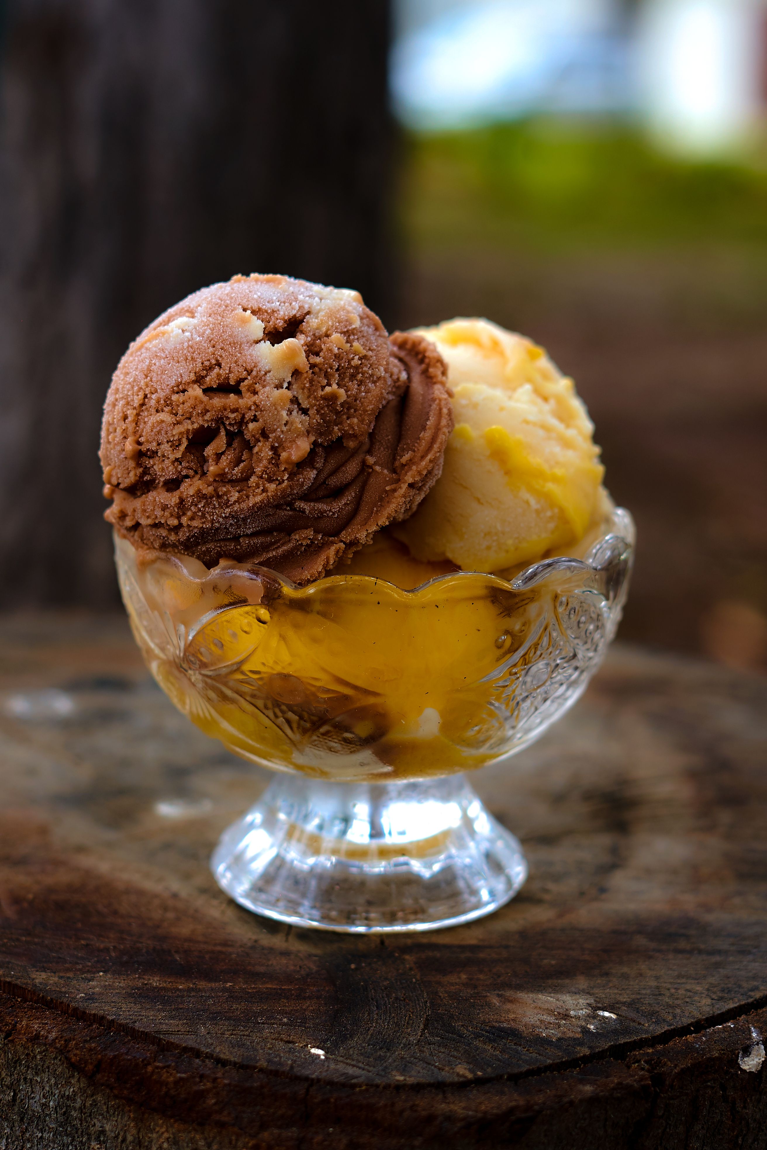 Indulge in a tasty frozen dessert with chocolate and mango scoops served in an elegant glass bowl.