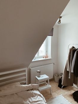 Minimalist bedroom featuring clothing rack, neutral tones, and natural light through a skylight.