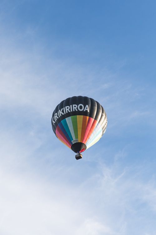 Free Vibrant hot air balloon with 'KIRIKIRIROA' lettering floats above Hamilton, NZ's clear sky. Stock Photo