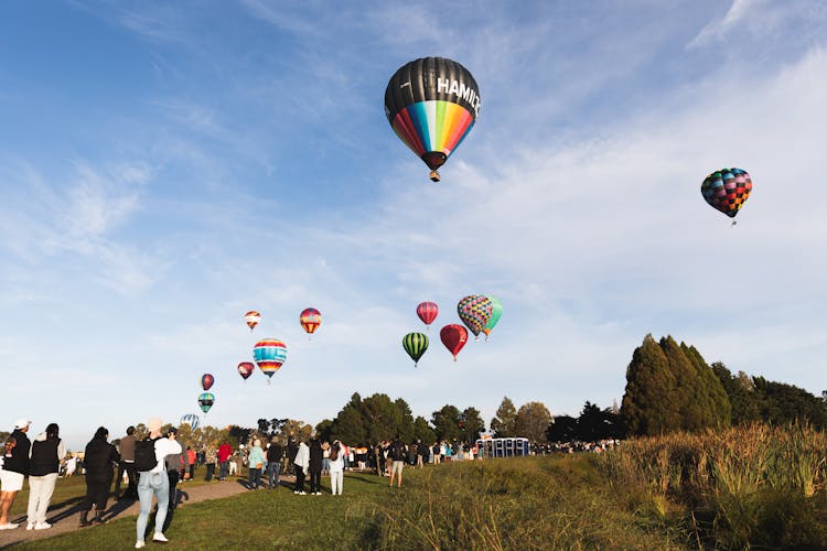 People Watching Hot Air Balloons Flying In Sky