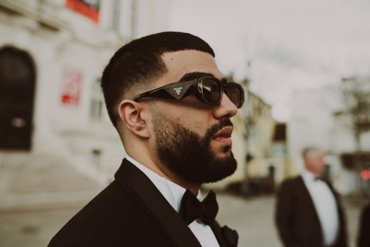A fashionable man wearing sunglasses and a suit in a Paris street, exuding confidence.