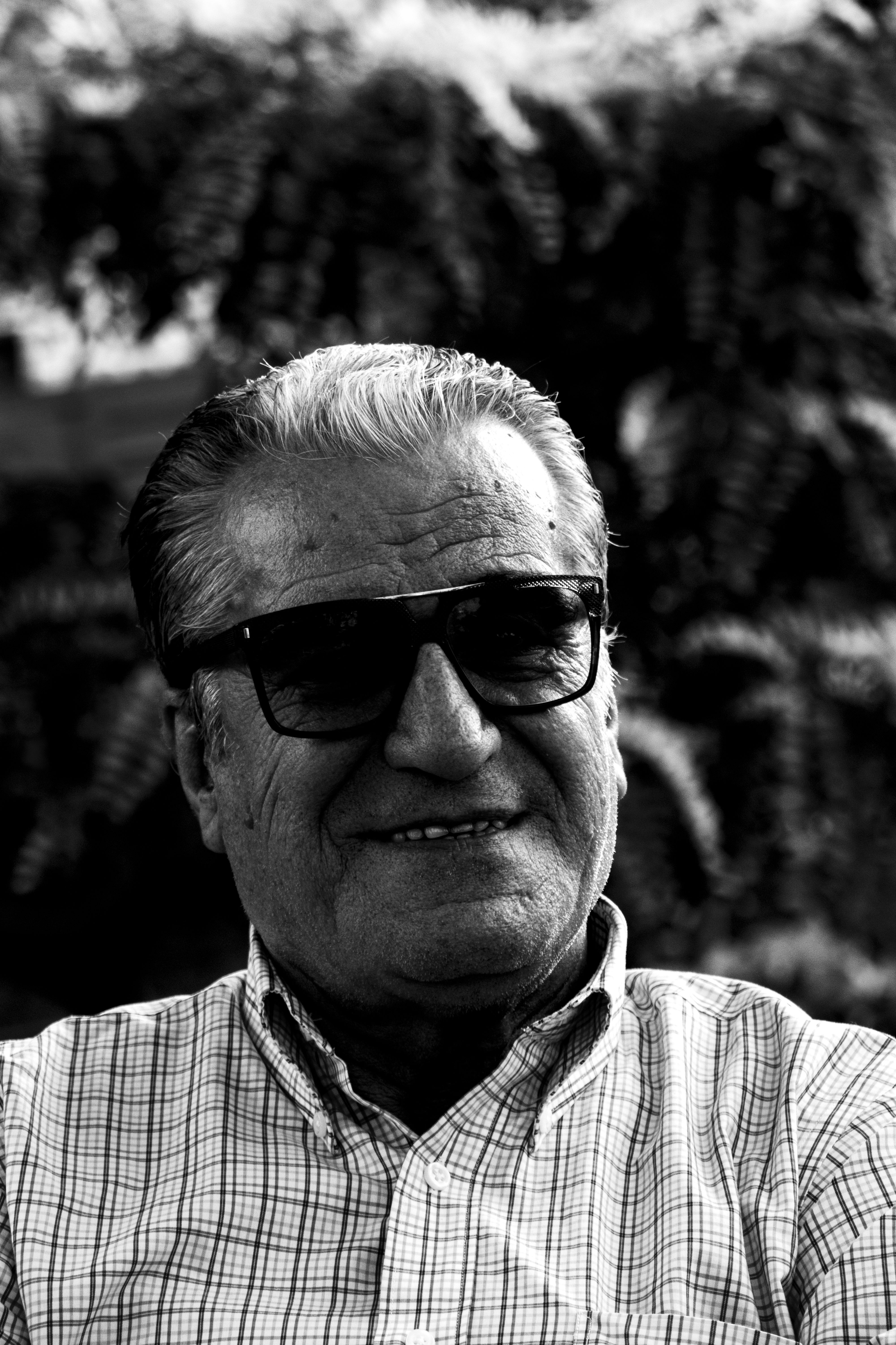 Portrait of a senior man smiling in black and white with checkered shirt and sunglasses.