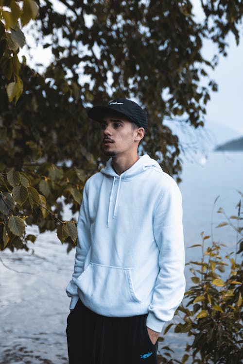 Young Man in White Hoodie and Baseball Cap by the Lake