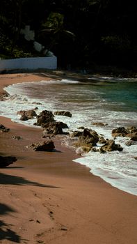 Tranquil beach scene with rocks, ocean waves, and golden sand under a clear sky.