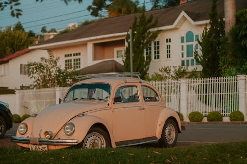 A Vintage, Pink Volkswagen Beetle Parked in front of a House 