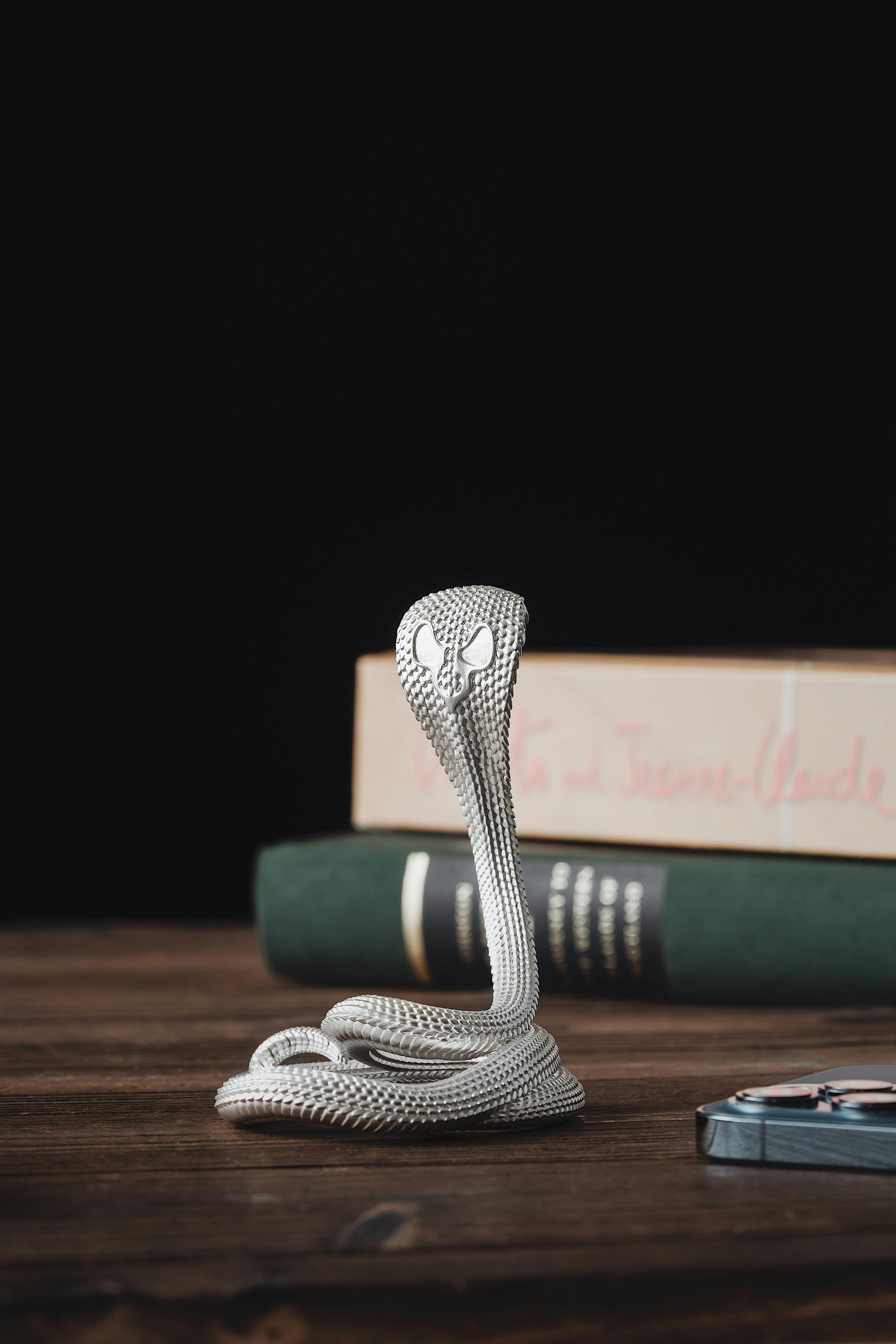 Handcrafted metal cobra sculpture serves as a stylish phone stand on a wooden desk.