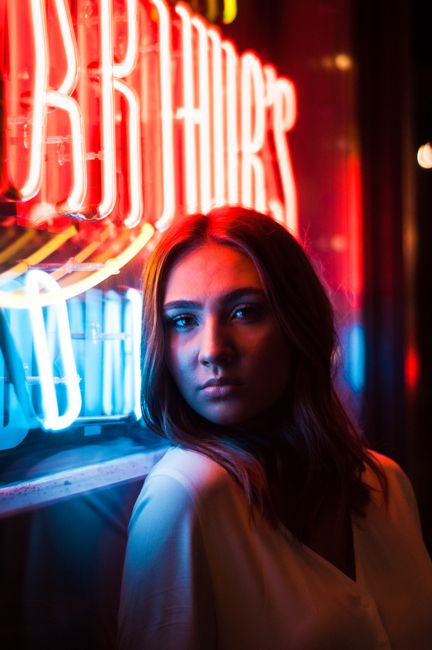A serious woman stands by neon lights at night, creating a colorful and urban mood.
