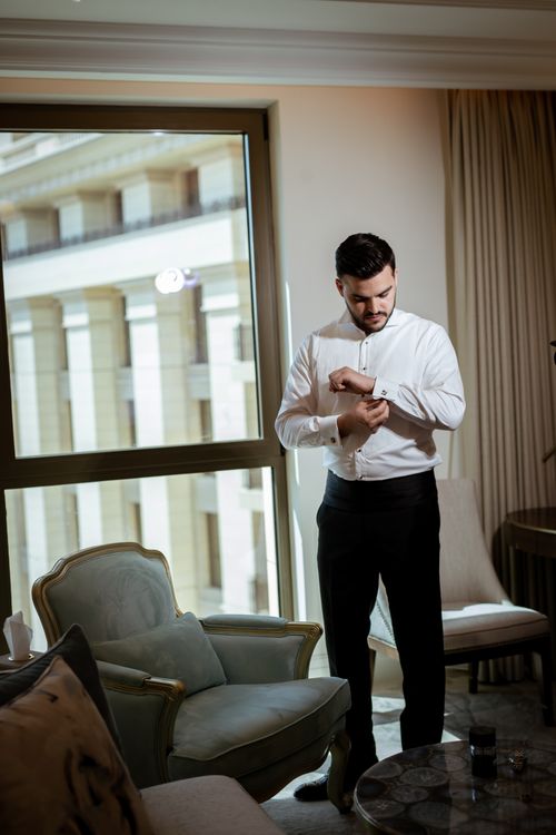 Free Man standing in a modern room adjusting cufflinks, showcasing elegance and fashion sense. Stock Photo