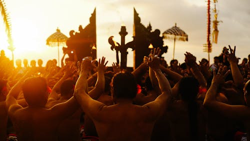 Back View of People Standing with Arms Raised at Sunset in Event