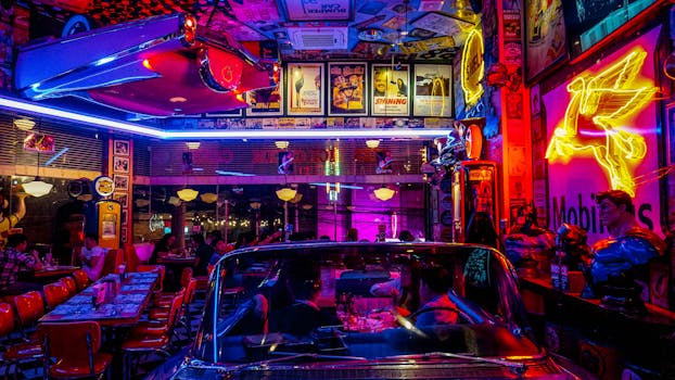 A lively retro diner bustling with people, neon lights, and classic car decor, set at night.
