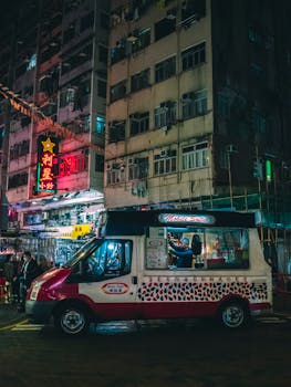 Dynamic urban night scene with a food truck, neon lights, and bustling city streets in Hong Kong.