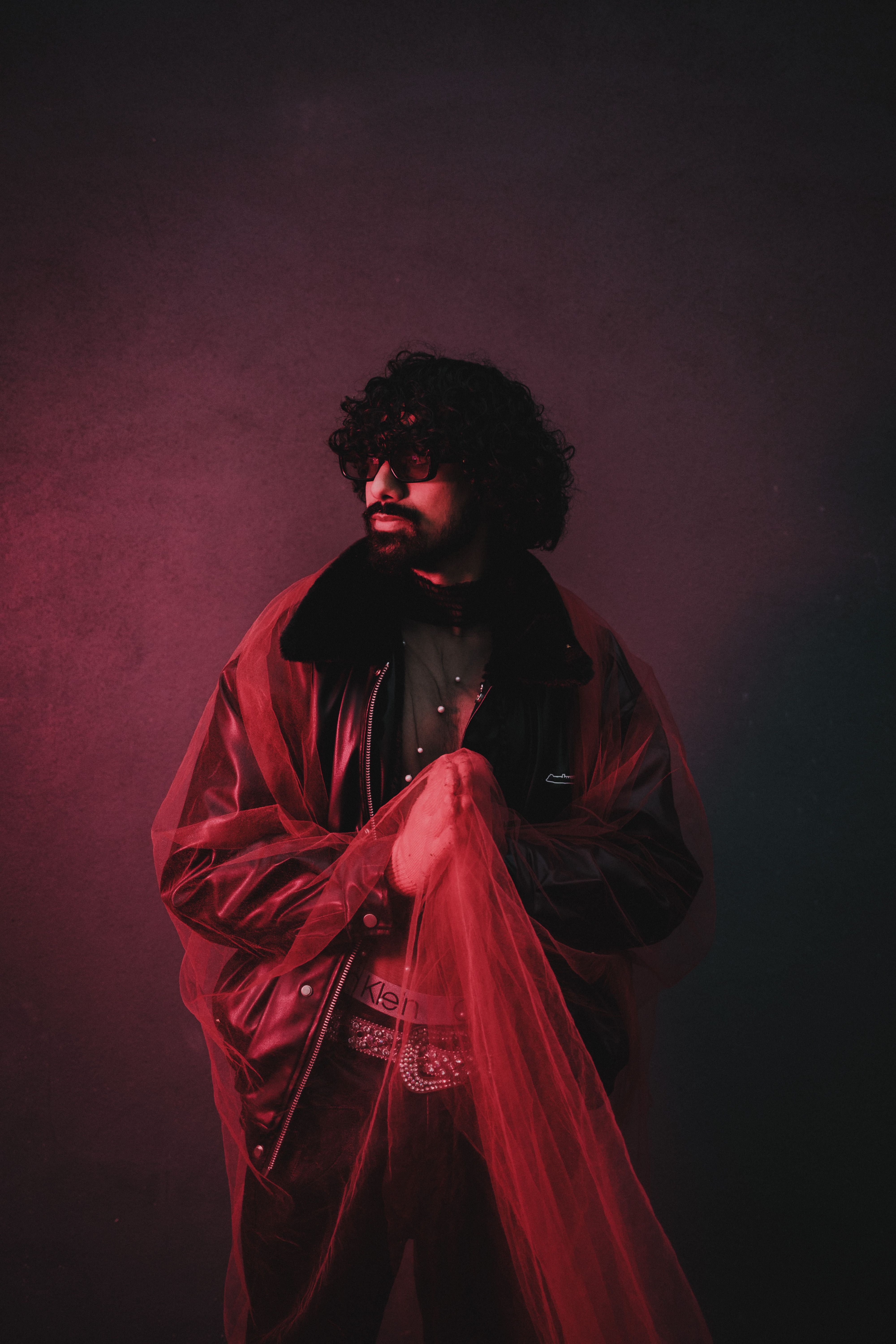 Artistic portrait of a man with curly hair in a red jacket holding fabric, emphasizing fashion.