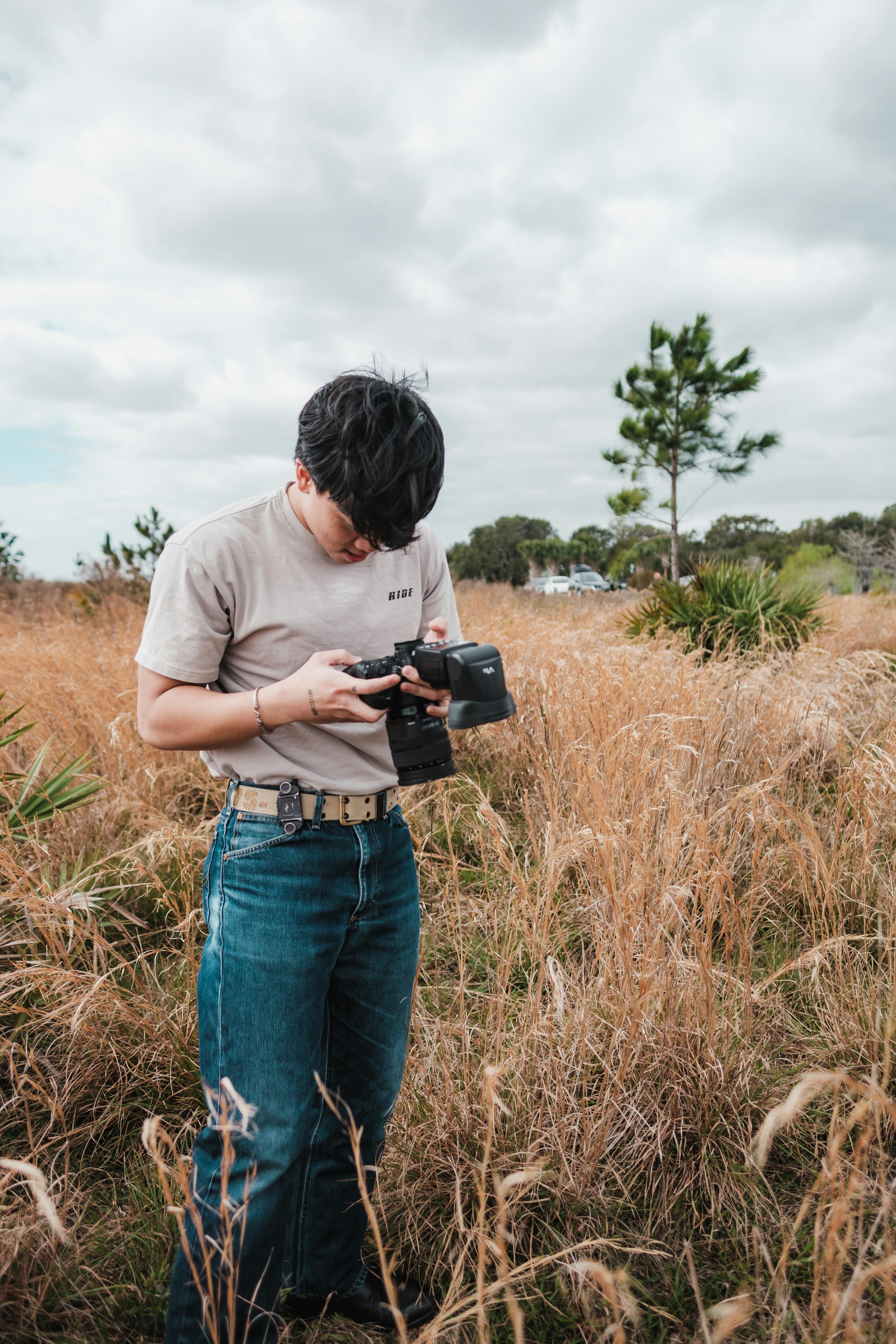 A photographer inspecting their camera in a grassy field under an overcast sky.
