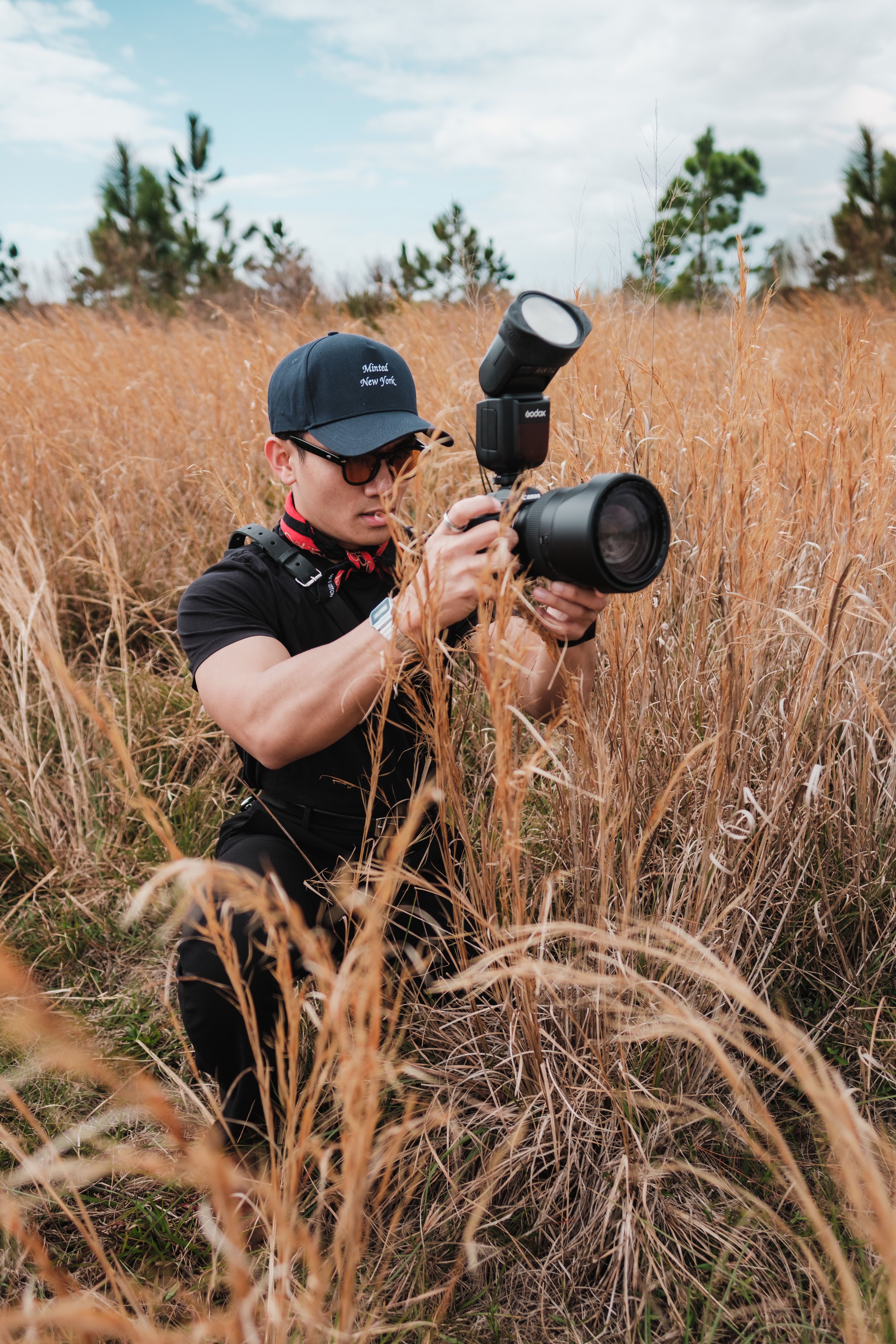 Photographer crouching in tall grass with DSLR camera capturing outdoor shots.