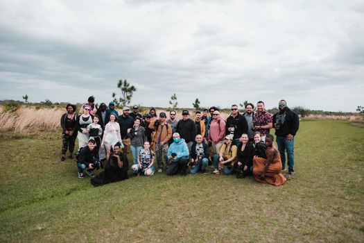 A diverse group of people posing together in an open field under cloudy skies, capturing a moment of camaraderie.