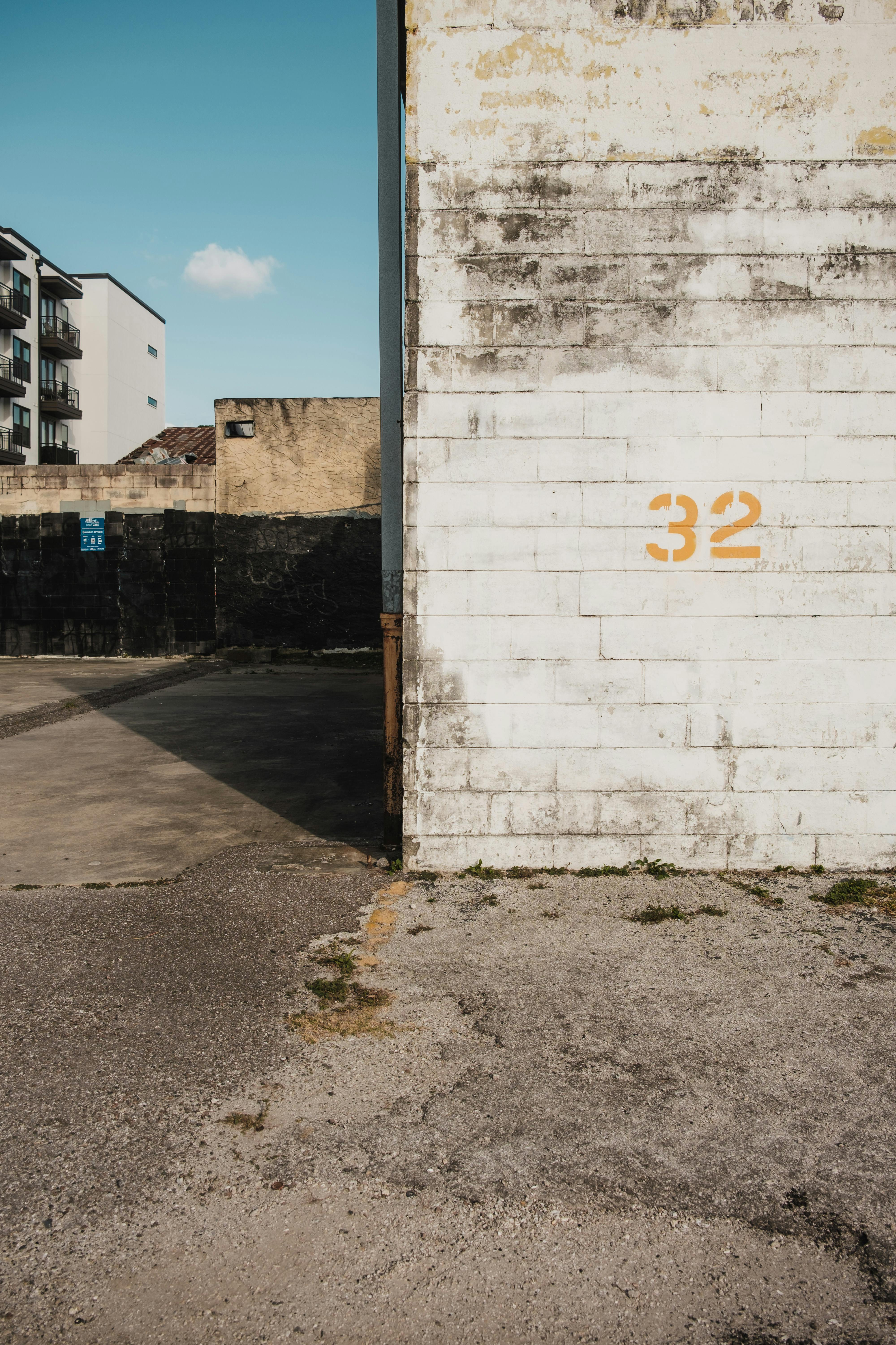 Free A sunlit urban scene showing a weathered building with the number 32 on a brick wall. Stock Photo