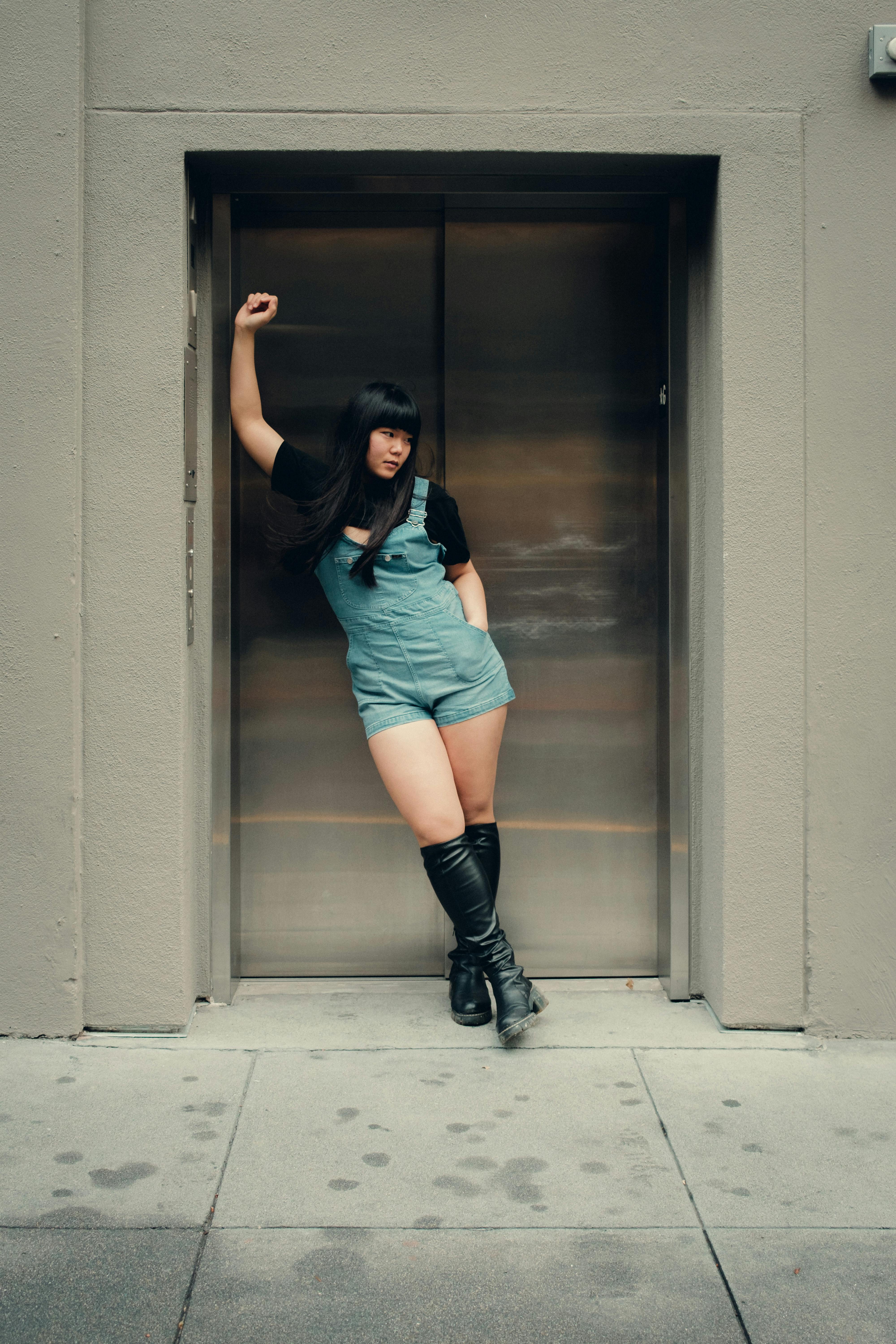 Asian woman striking a stylish pose in a building elevator, showcasing modern urban fashion.