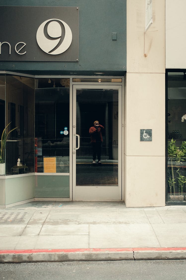 Man Taking Picture In Shop Glass Doors Reflection